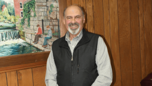 Jordan Mayor Richard Platten stands by one of his favorite paintings depicting boys fishing in Skaneateles Outlet.